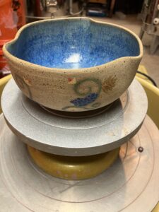 A large bowl with a glossy flux blue glaze on the inside. The outside has been left raw with hand painted fruits painted on the outside.