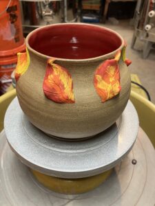 A beautiful large vase with raw clay exterior and vibrant orange, yellow, and red hand painted foliage on the outside. The inside has been finished with a deep, glossy red.